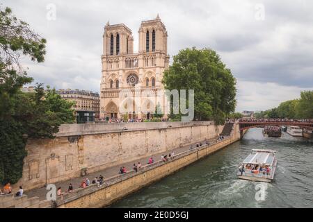 Tourists and locals alike gather along the banks of the Seine River in front of the famous Notre Dame cathedral. Stock Photo