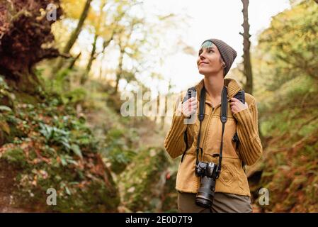 Low angle of traveling photographer standing in woods with photo camera and looking up while admiring nature during vacation Stock Photo
