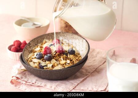Hand with a jug pouring milk to granola with berries Stock Photo