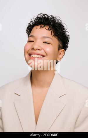 Young Latina Woman with Asian eyes smiling and wearing a beige blazer, isolated vertical photo, white background