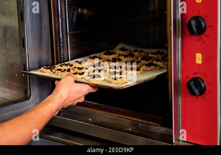 Crop anonymous baker putting baking sheet with sweet cookies with fruits into hot oven while working in industrial kitchen Stock Photo