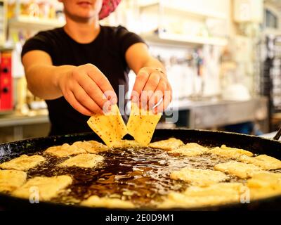 Crop unrecognizable female chef putting pieces of dough into boiled oil while preparing deep fried pastry in kitchen Stock Photo