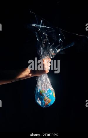 Unrecognizable crop person with Earth globe in plastic bag on black background showing concept of planet pollution Stock Photo