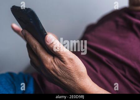 Senior ethnic male in glasses relaxing on couch in living room and reading messages on smartphone Stock Photo