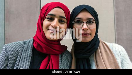 Charming Arab female friends wearing traditional hijab standing in city while smiling and looking at camera Stock Photo