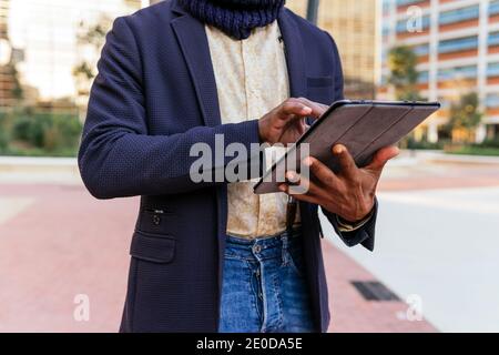 Cropped unrecognizable busy African American male freelancer standing in the street browsing on tablet while working remotely on project Stock Photo