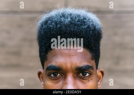 Crop determined African American male with dyed curly hair standing in city and looking at camera Stock Photo