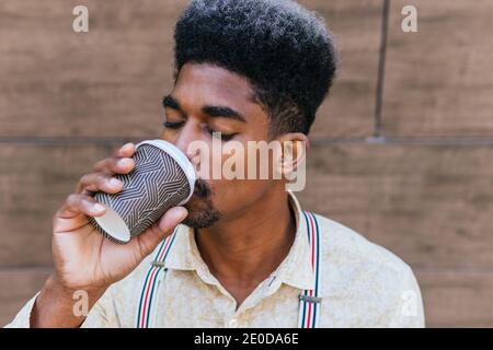 Delighted black male drinking coffee from disposable cup of takeaway with eyes closed Stock Photo