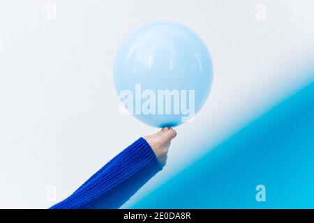 Unrecognizable crop female in knitted sweater standing on white background with blue air balloon Stock Photo