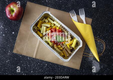 From above of delicious macaroni with ketchup and cheese placed in container for takeaway food on table with apple Stock Photo