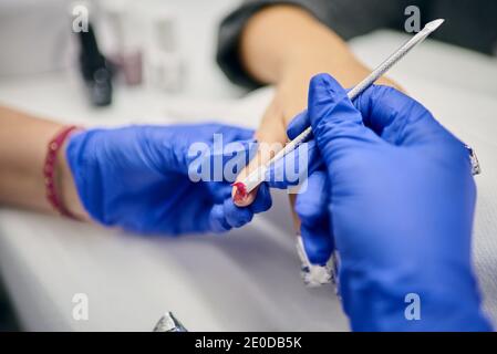 Crop master of manicure using metal spatula and removing gel polish from nails of client in beauty salon Stock Photo