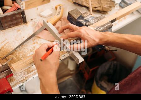 From above of crop faceless male carpenter using metal angle and wooden plank while working at workbench in bright garage Stock Photo