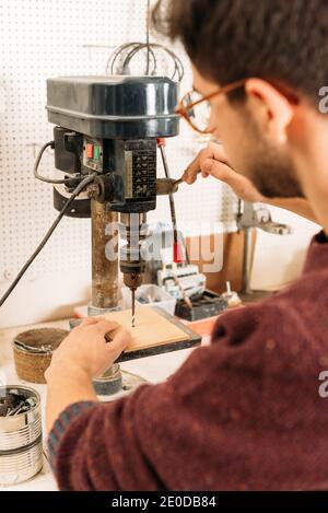 Side view of male woodworker using drilling tool while working with wood in bright carpentry workshop Stock Photo