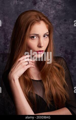 Calm female model in stylish clothes standing in studio with red hair and looking at camera Stock Photo