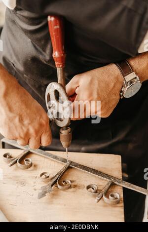 Crop anonymous artisan using old hand drill while working with ornate wooden detail in workshop Stock Photo