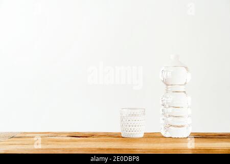 Empty glass and plastic bottle filled with pure fresh water placed on wooden table against white wall Stock Photo