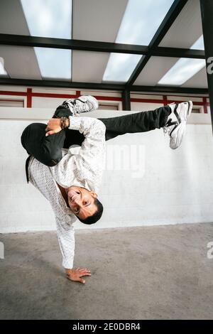 Full body of energetic young man doing acrobatic handstand while performing break dance Stock Photo