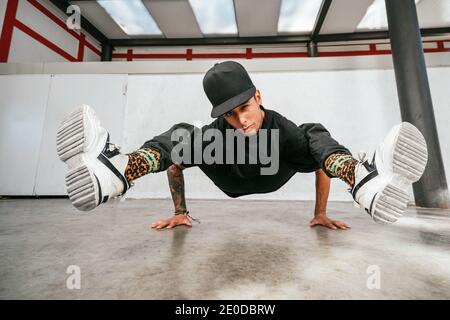 Full body of energetic young man doing acrobatic seated while performing break dance Stock Photo