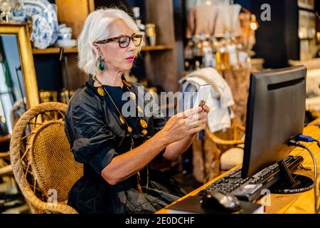Side view of mature female entrepreneur in elegant dress sitting at table and typing on keyboard while working on computer on project online Stock Photo