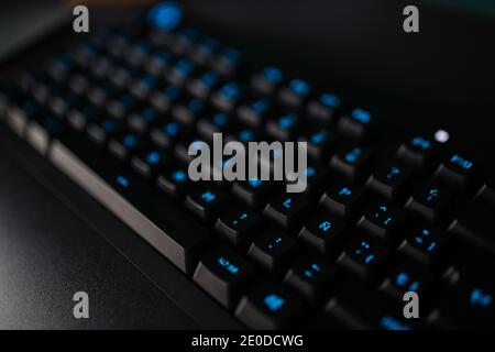From above of black keyboard with blue illuminated letters placed on desk near computer monitor Stock Photo