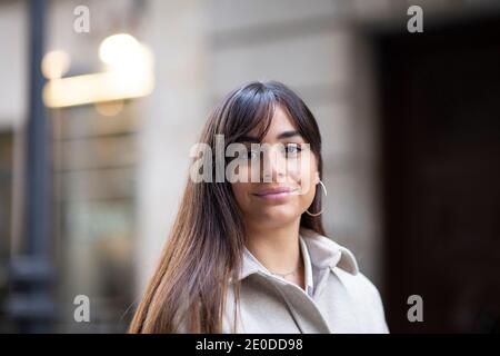 Gorgeous young ethnic female with long dark hair in casual outfit smiling and looking at camera on city street Stock Photo
