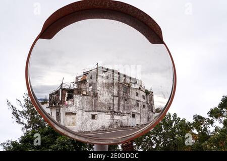 Shabby abandoned building reflecting in convex mirror located on road on East Coast Stock Photo