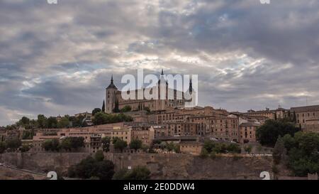 Aerial view of old city with historic buildings and stone castle on hill against cloudy sky during sunset in Toledo, Spain Stock Photo