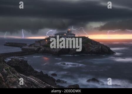 Picturesque view of thunderstorm with flashes of lightnings above lonely house on island in stormy sea at sunset Stock Photo