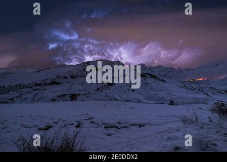 Scenery of mountain range covered with snow under thunderstorm sky with bright lightnings in winter Stock Photo