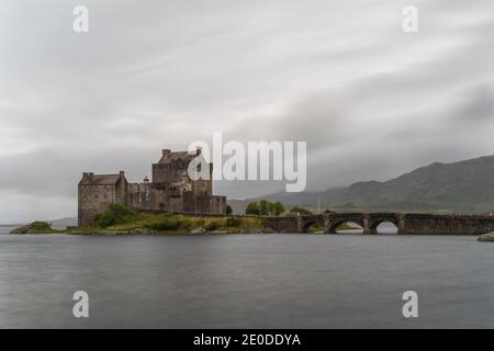 Ancient Eilean Donan Castle with old stone bridge on overcast day in mountainous area in Scotland Stock Photo