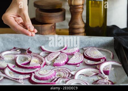 Unrecognizable chef adding seasonings on chopped onions placed on baking paper on pan in domestic kitchen and cooking delicious dish Stock Photo