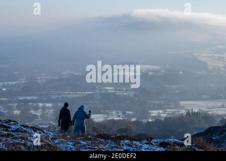 UK weather - 31 December 2020: Snow sunshine and light mist add festive cheer to Burley Moor in Wharfedale on New Year's Eve. Two people walk a dog along the edge of Burley Moor in stunning wintry conditions. West Yorkshire Rebecca Cole/Alamy News (c) Stock Photo