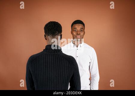 Back view of ethnic man standing in studio with African American male looking confidently at camera on brown background Stock Photo