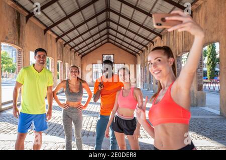 Group of diverse runners in sportswear standing in street and taking selfie on smartphone during workout in summer Stock Photo