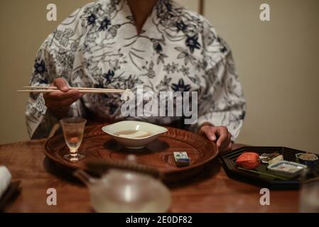Close up view of hands of female caucasian Woman in kimono using chopsticks to eat Japanese food at ryokan Stock Photo
