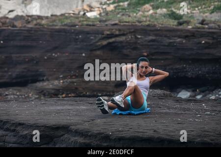 Determined sportsWoman doing abs exercises while balancing on beach near sea during workout Stock Photo