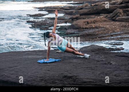 Determined female athlete balancing in side plank while doing exercises during workout at seaside Stock Photo