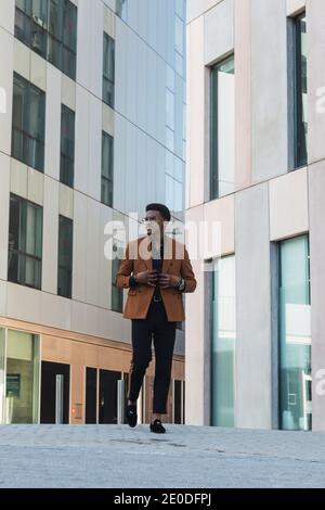 Front view of young handsome black guy in trendy suit and eyeglasses while walking in modern building hall Stock Photo