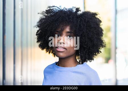 Beautiful young African American female with curly hair looking at camera while standing on the street Stock Photo