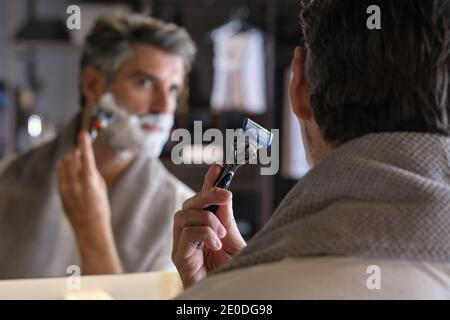 Stock photo of middle aged man with grey hair using shaving cream to shave his beard. Stock Photo