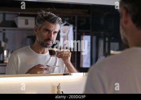 Stock photo of middle age man having a coffee and looking himself in the mirror. Stock Photo