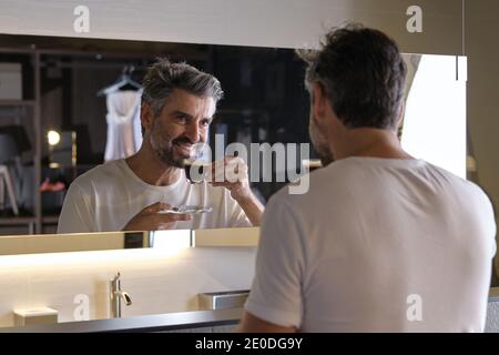 Stock photo of middle age man having a coffee and looking himself in the mirror. Stock Photo