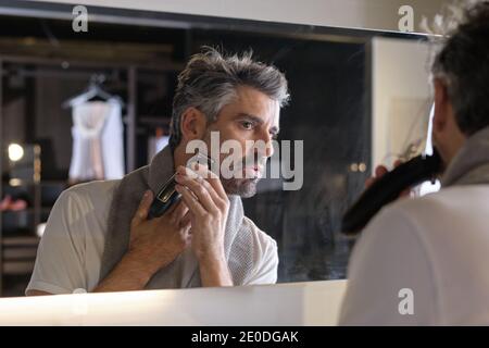 Stock photo of middle age man using beard trimmer in the bathroom. Stock Photo