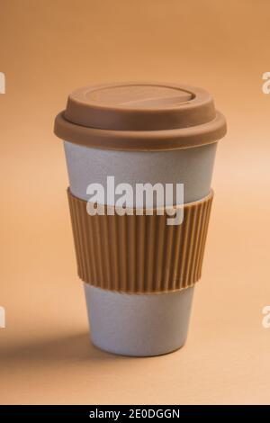 Minimalist white paper cup of takeaway coffee with brown silicone ring and lid against beige background Stock Photo
