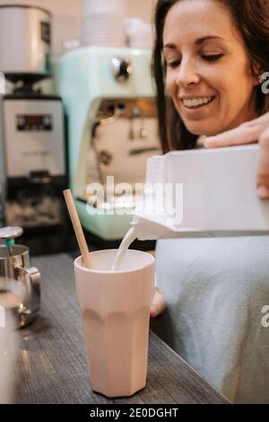 Smiling female bartender pouring milk into cup while preparing milkshake at counter in cafe Stock Photo