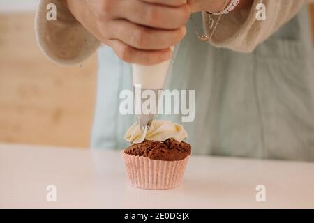 Crop anonymous confectionery chef using pastry bag while decorating cupcake with whipped cream Stock Photo