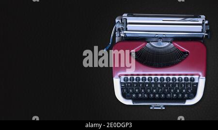 Mechanical typewriter on the right against a horizontal dark gray background. Red metallic type machine with copy space for text. News concept. Stock Photo