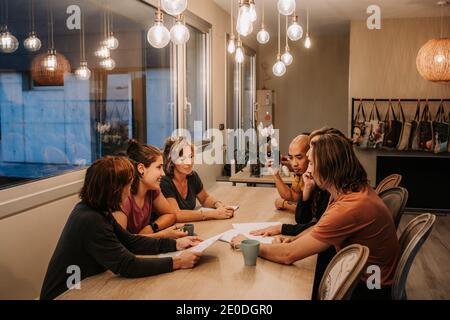 Company of people sitting together at table with papers and speaking about project while looking at each other Stock Photo