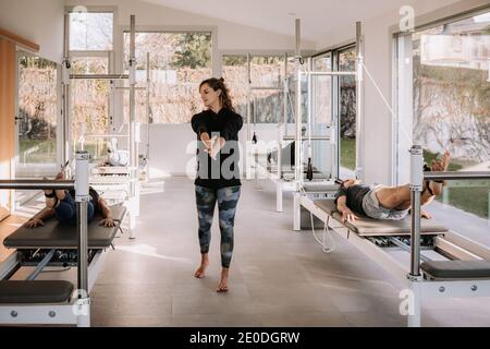 Group of people in sportswear lying on pilates machines with straps and doing exercises under supervision of professional trainer in gym Stock Photo