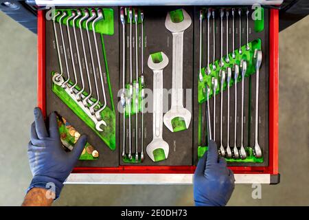 Top view of crop unrecognizable male technician standing near tool cabinet with collection of various spanners in car service Stock Photo